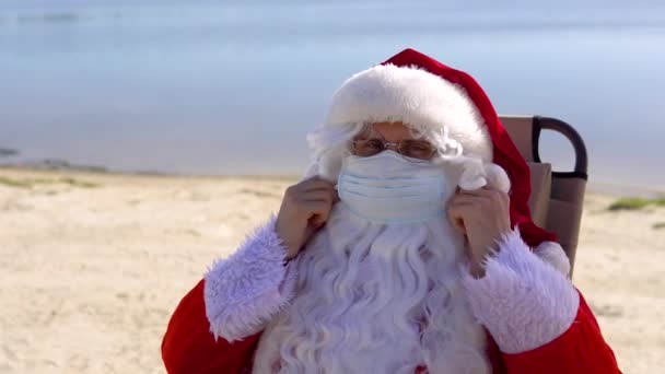 圣诞老人摘下了躺在沙滩上的防晒霜上的医疗面具 — 图库视频影像