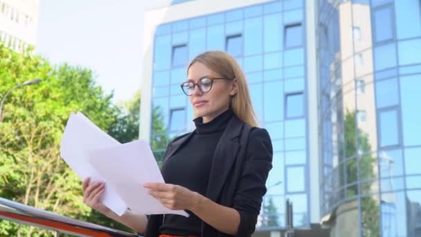 Giovane operaia in possesso di documenti in piedi sulla strada della città. Bella bionda che guarda i documenti, il giorno d'estate. Concetto: business — Video Stock