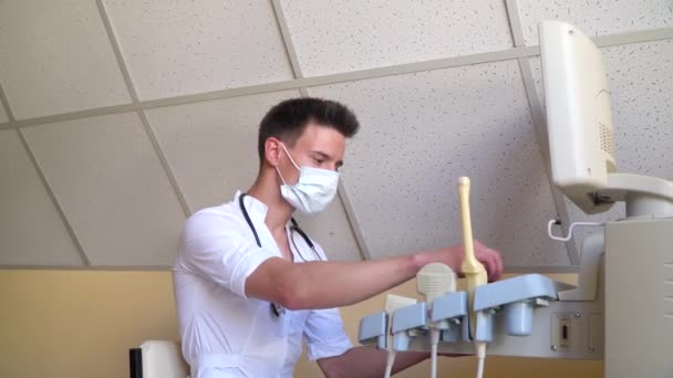 Diagnóza rakoviny prsu. Mladý lékař v ochranné masce vyšetřuje pacienta. Ultrazvukové přístroje monitorují detailní záběr. Držení zdravotnického vybavení — Stock video
