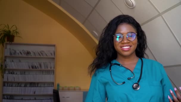 Retrato de uma médica afro-americana sorridente com óculos satisfeitos com seu hospital de trabalho. Conceito de medicina, cuidados de saúde e pessoas — Vídeo de Stock