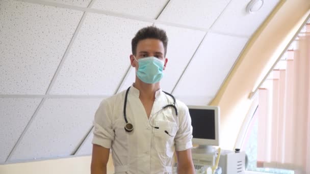 Porträt eines professionellen Arztes mit Stethoskop in Schutzmaske. Krankenhaus mit Ultraschallgeräten im Hintergrund — Stockvideo
