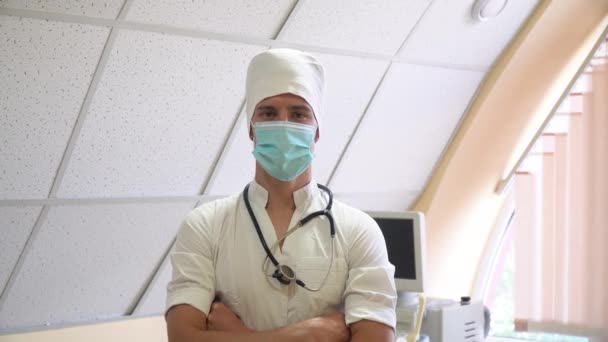 Retrato de médico profesional con estetoscopio en máscara protectora. Hospital con dispositivos de ultrasonido en segundo plano — Vídeos de Stock