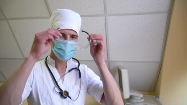 Junger Arzt in medizinischer Maske setzt im Krankenhaus eine Brille auf. Vorbereitung auf die Operation — Stockvideo