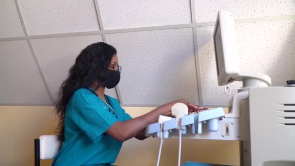 戴防护面罩的非裔美国女医生在超声波设备上工作。对怀孕的诊断 — 图库视频影像