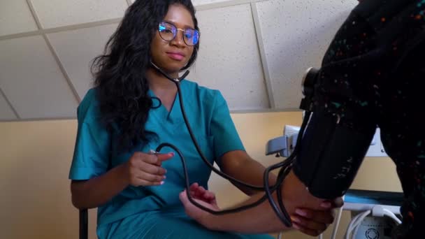 Médica afro-americana profissional sentada no hospital e medindo a pressão arterial de um paciente. Conceito de saúde e prevenção — Vídeo de Stock