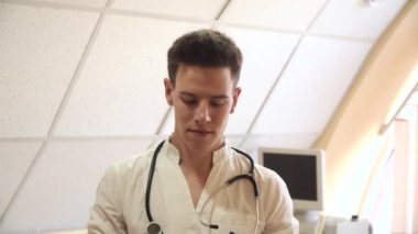 Genç doktor stajyer, arka planda ultrason cihazlarıyla hastanede maske takıyor. Karantinanın sonu