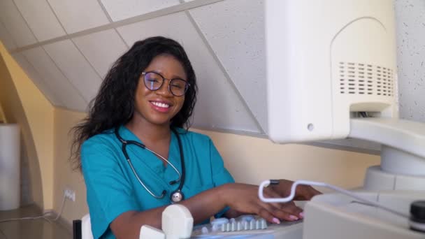 Улыбающийся африканский американский врач работает над ультразвуковым прибором — стоковое видео