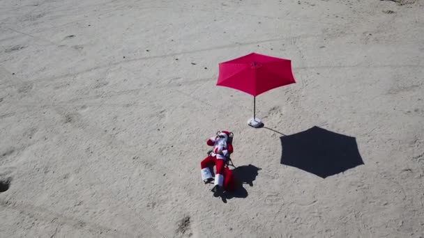 Санта Клаус лежит на шезлонге на песчаном пляже. Вид сверху. Расслабься Санта-Клаус в США — стоковое видео