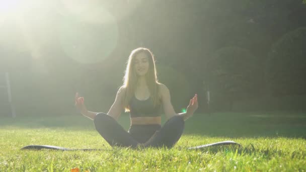 Młoda kaukaska kobieta relaksująca się ćwicząc jogę w parku nad jeziorem. Koncepcja zdrowego stylu życia — Wideo stockowe