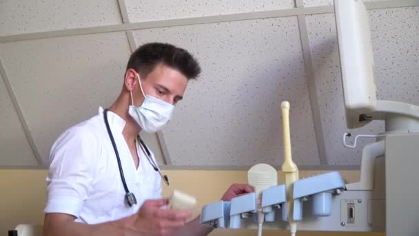 Médico joven en máscara protectora que trabaja en el dispositivo de ultrasonido. Diagnósticos covid 19 — Vídeos de Stock