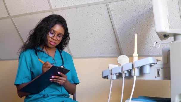 Afrikanischer Arzt mit einem Notizbuch in einem modernen Krankenhaus. Arzt untersucht die Krankengeschichte des Patienten. Konzept der Medizin, des Gesundheitswesens und der Menschen — Stockvideo