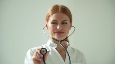İş yerindeki klinikteki beyaz önlüklü kadın doktorun yakın çekimi elinde steteskop tutuyor ve potansiyel hastanın nefes alışını dinliyor. Kadın doktor steteskop kullanıyor.