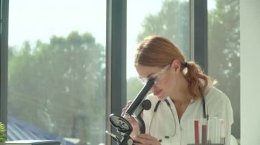 Kadın bilim adamı doktor biraz araştırma yapıyor ve laboratuvarda mikroskoba bakıyor. Kan testi. Covid 19 testi
