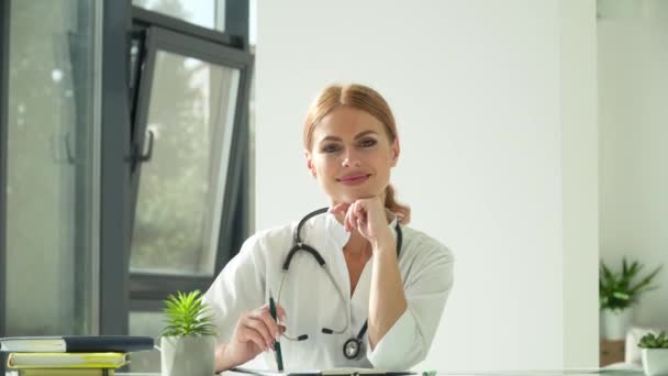 Glückliche junge kaukasische Ärztin in weißem Arztkittel und Stethoskop, die in die Kamera blickt. Lächelnde Ärztin posiert im Krankenhausbüro — Stockvideo
