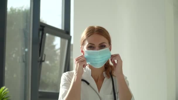 Молодая белая женщина-врач снимает медицинскую маску для лица в больнице — стоковое видео