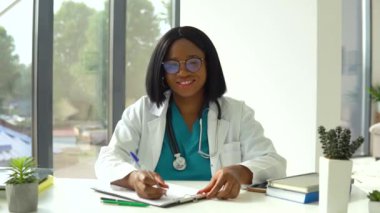 Gülümseyen Afro-Amerikan kadın doktor hastane ofisinde poz veriyor.