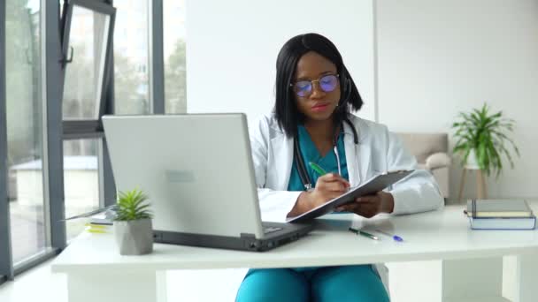 Professionele Afrikaanse Amerikaanse vrouwelijke arts in witte medische jas en headset maken conference call op laptop computer, consulting afstand patiënt online in video chat — Stockvideo