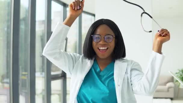 Happy young african american woman doctor dancing with a stethoscope in the hospital — Stock Video