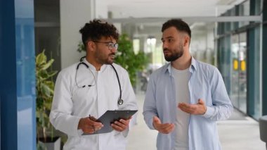 Görüntüler, elinde steteskop ve pano olan bir doktorun hastane koridorunda belirtileri açıklarken dikkatle dinlediğini gösteriyor.