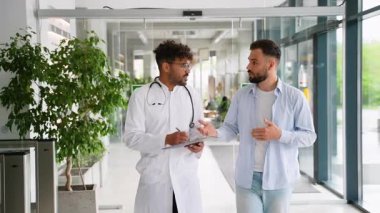 Steteskop takan ve pano tutan profesyonel bir tıp uzmanı. Hastanenin koridorunda yürürken hastanın sağlık sorunlarını dikkatle dinliyor.