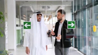Geleneksel beyaz elbiseli başarılı Arap işadamı ve modern ofis binasında yürüyen ve konuşan siyah takım elbiseli batılı iş adamı.