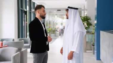 Biri batı takım elbiseli iki işadamı ve diğeri geleneksel ortadoğu kıyafetleriyle bir tartışmaya girişiyor ve çağdaş bir ofis ortamında el sıkışarak bitiriyorlar.