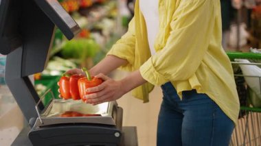 Müşteri markette kırmızı biberleri dijital olarak tartıyor, etiketi basıyor ve alışveriş arabasına koymadan önce ürünlerin üzerine yerleştiriyor.