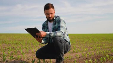 Tarım uzmanları büyümeyi ve ekinlerin sağlığını gözlemler, geniş ekili bir alanın ortasındaki bir panoya gözlemleri özenle kaydeder.
