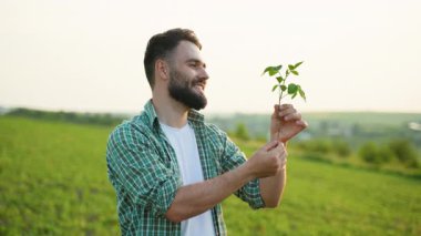 Deneyimli çiftçi yeşil tohumu dikkatlice inceliyor, verimli tarım arazilerinde duruyor, sürdürülebilir ekin ekimine olan tutkusunu gerçek bir gülümsemeyle gösteriyor.