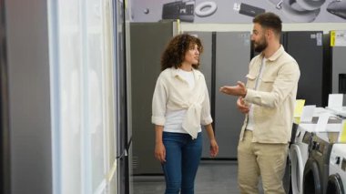 Kadın müşteriye buzdolabı seçimi yoluyla rehberlik eder, modern elektronik mağazası alanında birden fazla seçeneği incelerken profesyonel tavsiyeler sunar