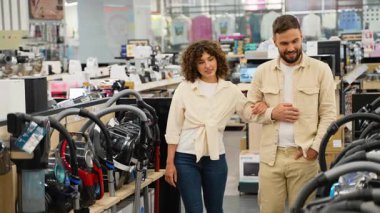 Genç bir aile elektronik mağazasından yeni bir elektrikli süpürge seçiyor. Bir kadın kocasına sevdiği bir modeli gösteriyor ve satın almayı tartışıyorlar.