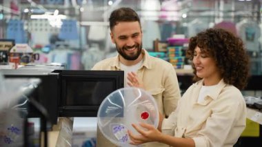 Neşeli ortaklar mikrodalga özelliklerini inceliyor, seçenekleri karşılaştırıyor ve modern perakende elektronik mağazasında yeni mutfak aletleri alırken heyecan verici ifadeleri paylaşıyorlar.