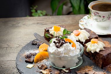 Cam kasede krema, çikolatalı pasta ve masada bir fincan kahve.