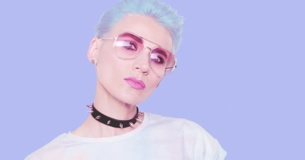 Mode Esthetisch alternatief Meisje met blauw kort haar, stijlvolle choker en zonnebril poserend in de studio tegen een blauwe achtergrond. Modeemoties, kapsel en accessoires concept — Stockvideo