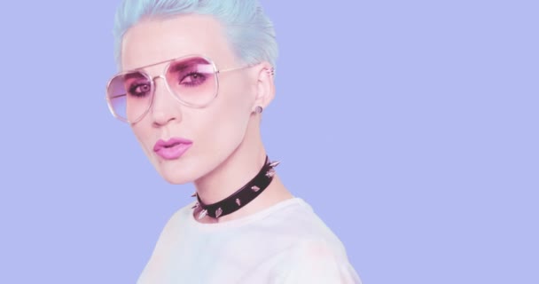 Αισθητική εναλλακτική λύση Κορίτσι με μπλε κοντά μαλλιά, κομψό τσόκερ και γυαλιά ηλίου ποζάρουν στο στούντιο με φόντο το μπλε. Συναισθήματα μόδας, χτένισμα και αξεσουάρ έννοια — Αρχείο Βίντεο