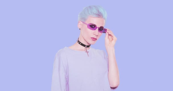 Ästhetische Alternative Mädchen mit blauen kurzen Haaren und stylischem Casual-Look posiert im Studio vor blauem Hintergrund. Mode-Emotionen, Frisur und Accessoires-Konzept — Stockvideo