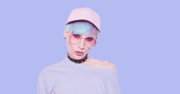 Módní alternativa Dáma s modrými vlasy, stylové sluneční brýle a čepice pózující ve studiu na modrém pozadí. Urban stylový vzhled a příslušenství koncept — Stock video
