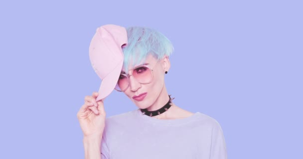 Moda łup Nastoletnia dziewczyna bawić się z niebieskimi włosami, stylowe okulary przeciwsłoneczne i czapka w studio na niebieskim tle. Urban stylowy wygląd i akcesoria koncepcja — Wideo stockowe