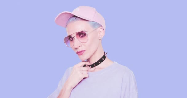 Moda Sexy Chica juguetona con el pelo azul, gafas de sol con estilo y la tapa posando en el estudio sobre fondo azul. Aspecto elegante urbano y concepto de accesorios — Vídeo de stock