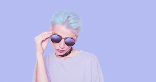 Fashion Girl z niebieskimi włosami i stylowe okulary przeciwsłoneczne pozowanie w studio na niebieskim tle. Moda stylowy wygląd i akcesoria koncepcji — Wideo stockowe