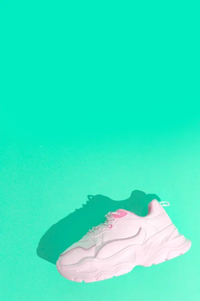 Minimal still life art. Fashion sport shoes concept. Aqua menthe trends. Stylish white sneakers on blue background