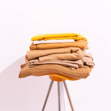 Sonbahar minimalist kompozisyonu. Odanın beyaz bölümündeki sandalyede bej rengi kahverengi elbiseler var. Sonbahar, sonbahar, kış konsepti. Moda hala yaşam blogcusu tarzı