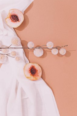 Beyaz tekstil arka planında taze şeftali ve dekor çiçekleriyle moda natürmortu. Asgari ruh hali estetiği.