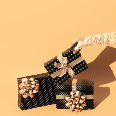 Altın bej arka planda izometrik olarak hediye kutusu polka dizaynı. Hediye, Noel tatili konsepti. Şık, durgun, el ele tutuşan altın eldivenli bir hayat sahnesi.