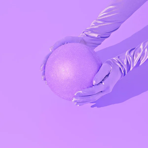 Minimal fashion still life scene. Gloved hand holds a ball. Stylish isometric space, Purple monochrome aesthetic. Holidays, christmas, winter, parties concept