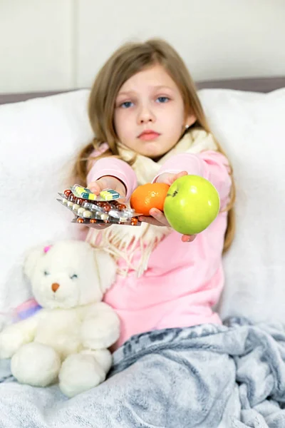 A sick little girl takes medication and eats fruit.