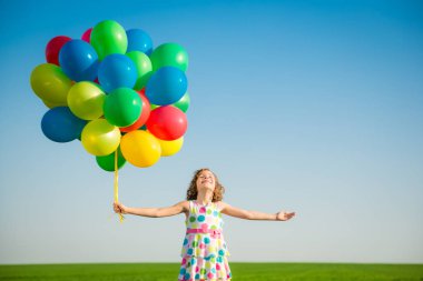 Mutlu çocuk açık havada parlak renkli balonlarla oynuyor. Çocuk mavi gökyüzü arka planına karşı yeşil bahar tarlasında eğleniyor. Sağlıklı ve aktif yaşam tarzı kavramı