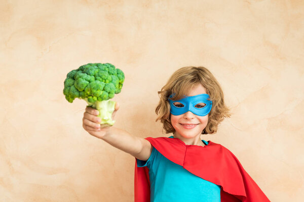 Superhero child eating superfood. Happy kid holding broccoli. Healthy eating and lifestyle concept. Green vegetarian food