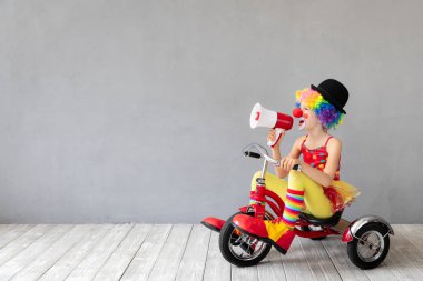 Komik çocuk palyaço evde megafon ve üç tekerlekli bisiklet, April Fools gün kavramı ile oynamak