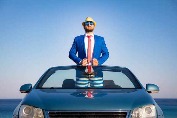 Успешный молодой бизнесмен на пляже. Мужчина, стоящий в классической кабриолете. Летние каникулы и свобода передвижения
